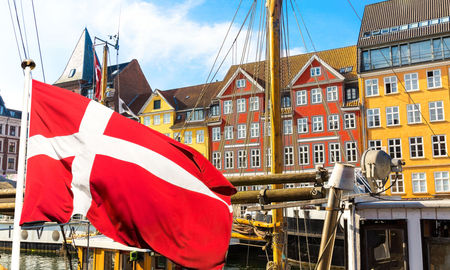 Denmark's national flag flying in the foreground of Copenhagen's famous old Nyhavn port.