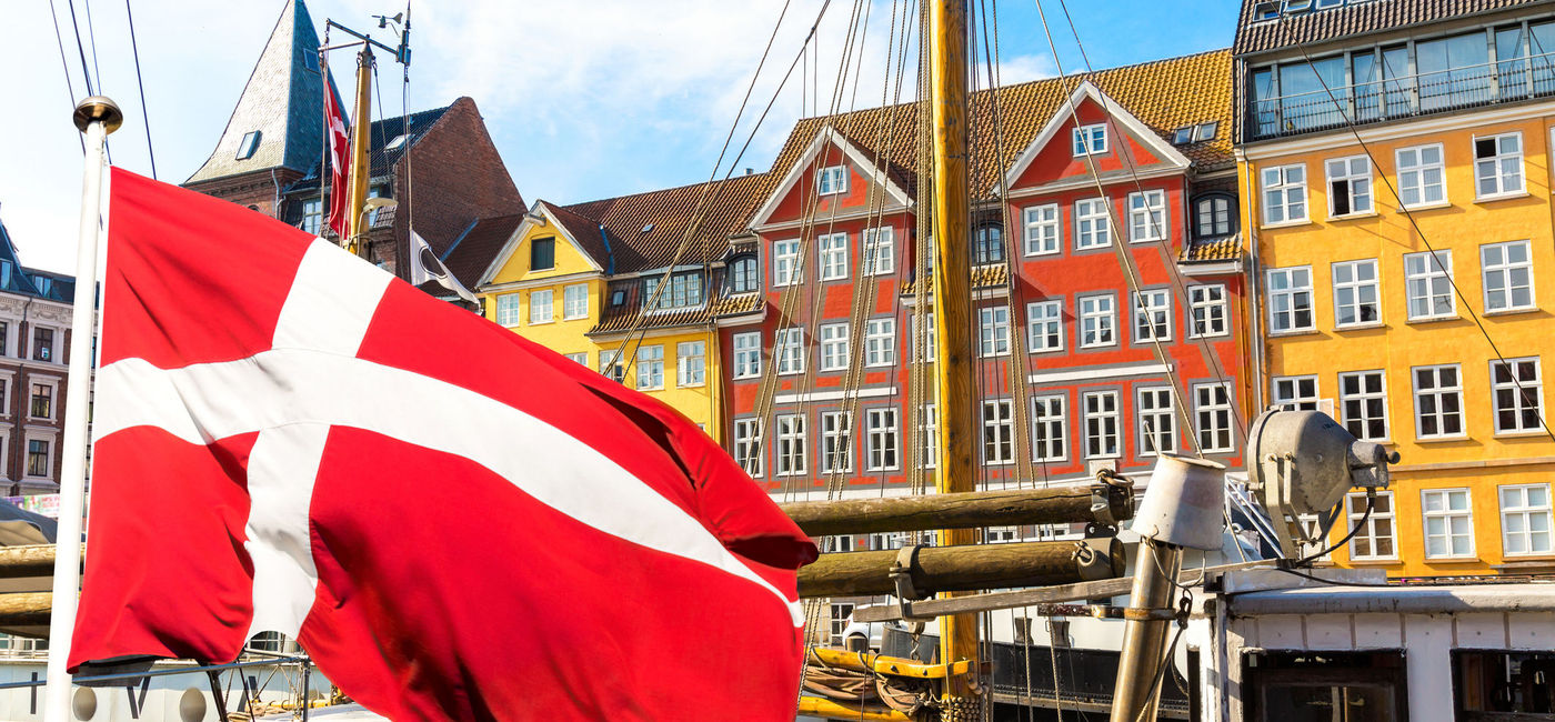 Image: Denmark's national flag flying in the foreground of Copenhagen's famous old Nyhavn port. (photo via iStock/Getty Images Plus/nantonov)